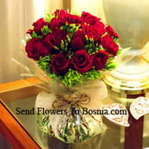 一束装有12朵红玫瑰和一些蕨类植物的花瓶